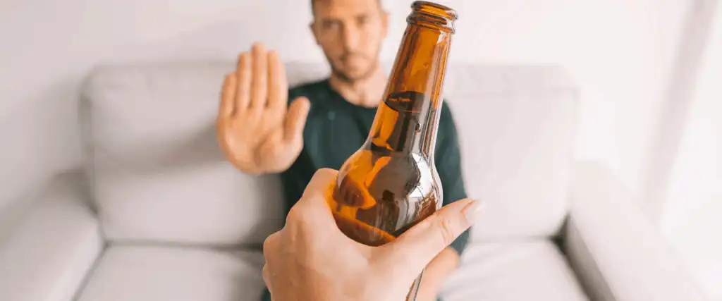 Man being offered a bottle of beer and holding his hand out refusing to take it