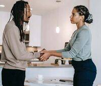 Man and woman holding hands and having a serious discussion in a modern kitchen, representing support during addiction recovery