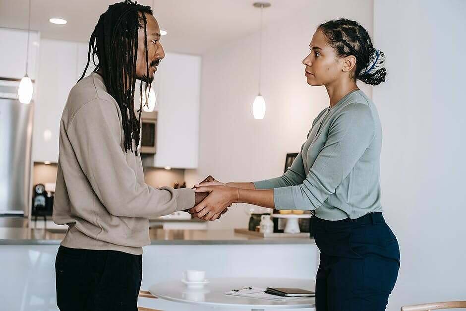 Man and woman holding hands and having a serious discussion in a modern kitchen, representing support during addiction recovery