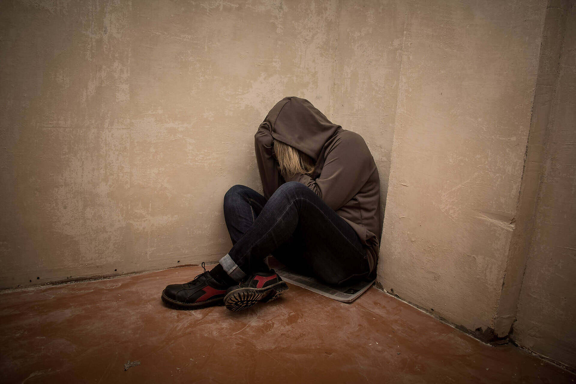 Person in hoodie sitting alone in corner, depicting depression and isolation often associated with addiction
