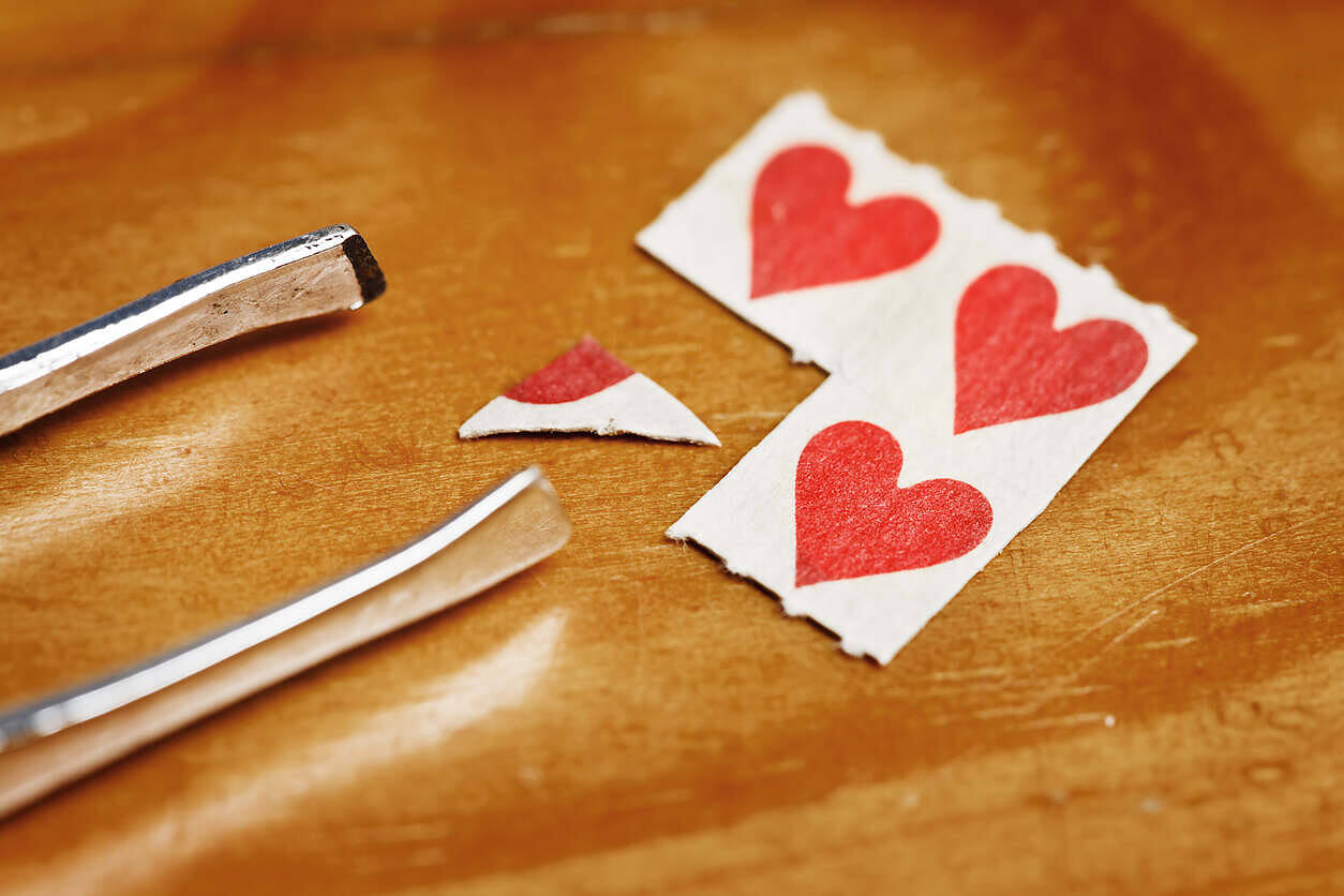 LSD blotter paper with red heart designs next to tweezers on a wooden surface, illustrating the deceptive nature of psychedelic drugs