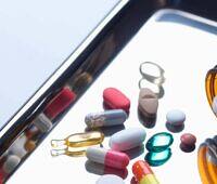 Various prescription pills and capsules scattered on a tablet screen next to an open medication bottle