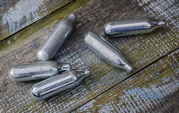 Several silver nitrous oxide canisters scattered on a weathered wooden surface, commonly used as a party drug known as 'laughing gas