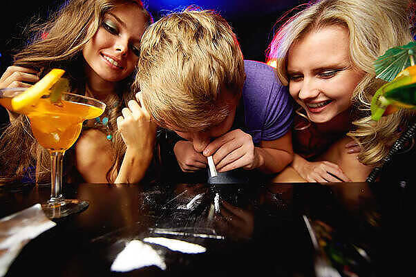 Young people using cocaine at a party, with alcoholic drinks visible, highlighting risks of party drug abuse