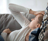 Young woman lying on couch with hand on forehead, appearing distressed, possibly experiencing withdrawal symptoms