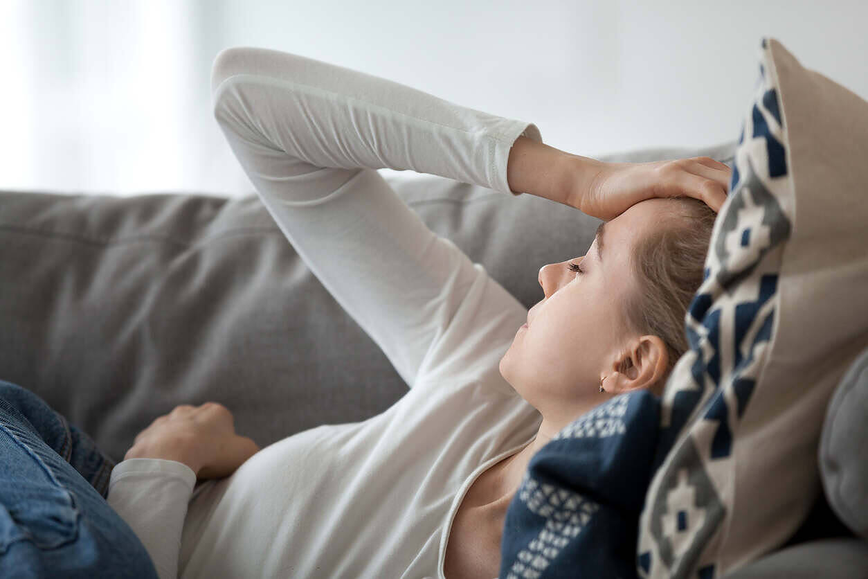 Young woman lying on couch with hand on forehead, appearing distressed, possibly experiencing withdrawal symptoms