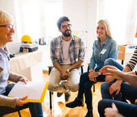 Diverse group of people sitting in a circle during a therapy session at an addiction treatment center, led by a female therapist