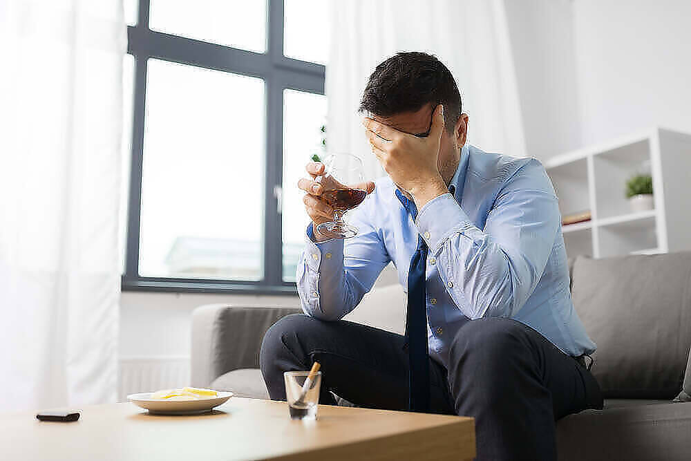 Stressed businessman holding wine glass, covering face with hand, displaying signs of alcohol addiction
