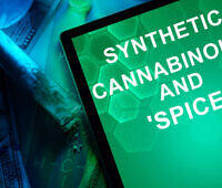 Tablet screen displaying "Synthetic Cannabinoids and 'Spice'" text with drug paraphernalia and money in the background