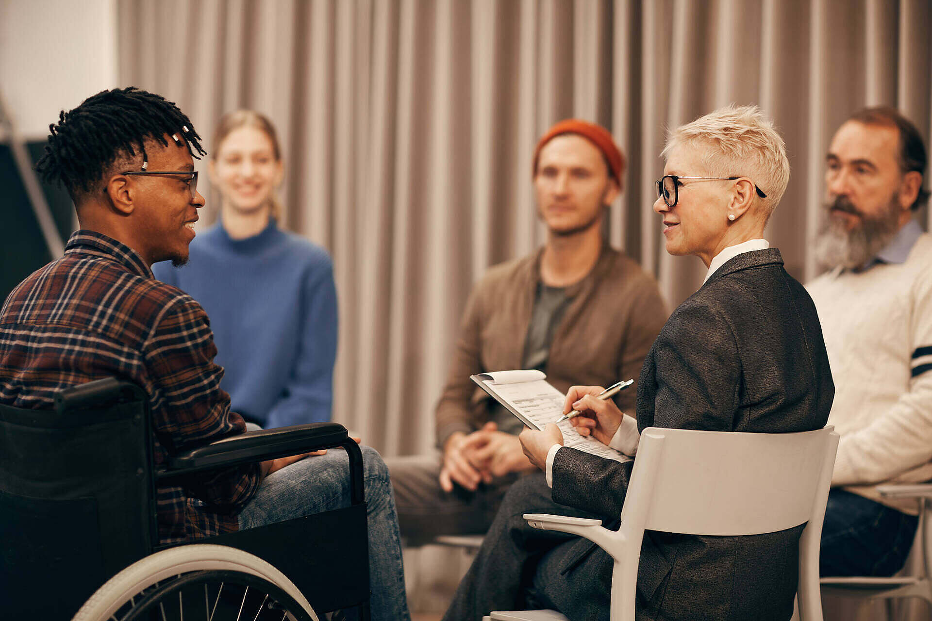 Therapist leading a diverse group therapy session, including a person in a wheelchair, for substance abuse treatment