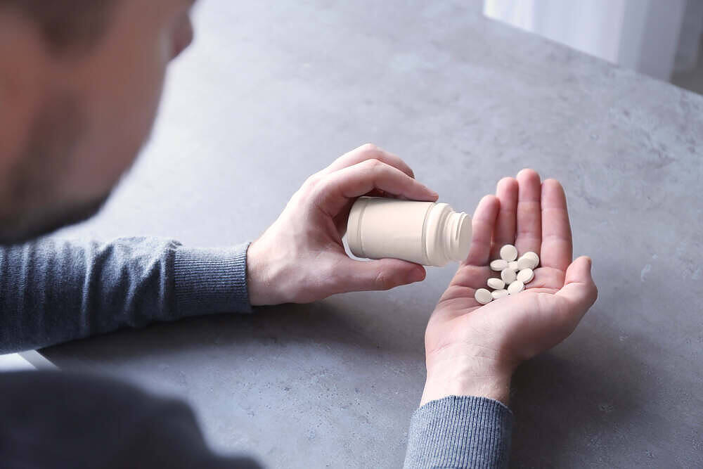 Man holding Mogadon pills and bottle, considering taking medication for sleep or anxiety