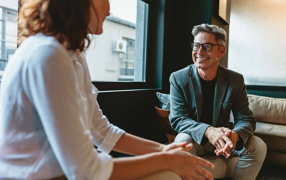 Smiling male therapist in glasses discussing naltrexone treatment with a female patient in a comfortable office setting