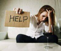 Distressed woman holding 'HELP' sign next to wine glass, illustrating struggle with alcoholism