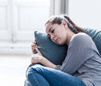 Distressed woman hugging pillow on couch, exhibiting signs of withdrawal during addiction recovery process