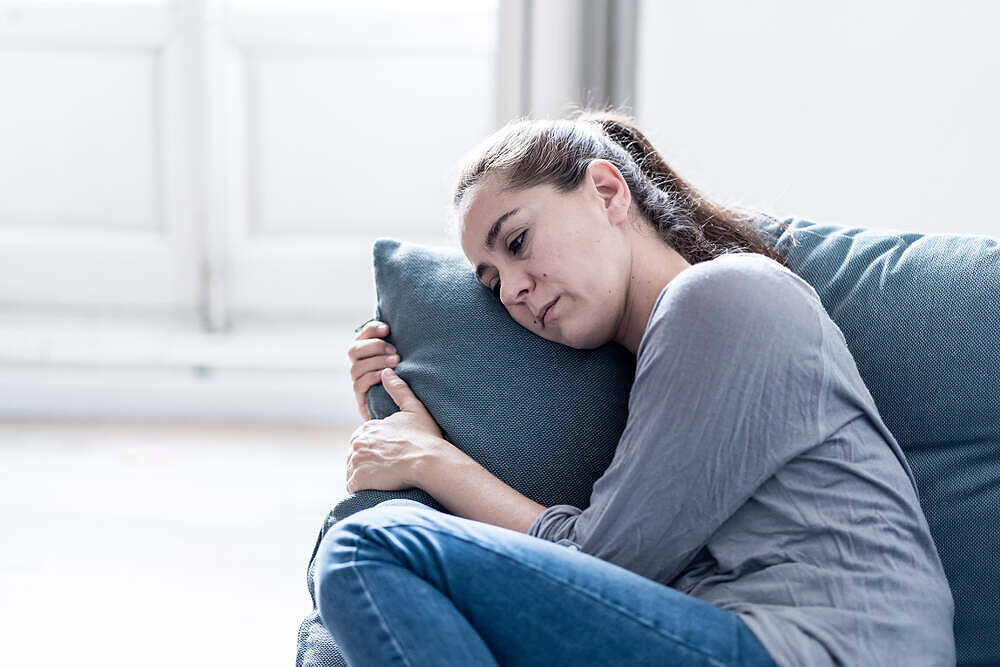 Distressed woman hugging pillow on couch, exhibiting signs of withdrawal during addiction recovery process
