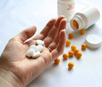Hand holding white pills with orange pills and medication bottles in background for addiction treatment