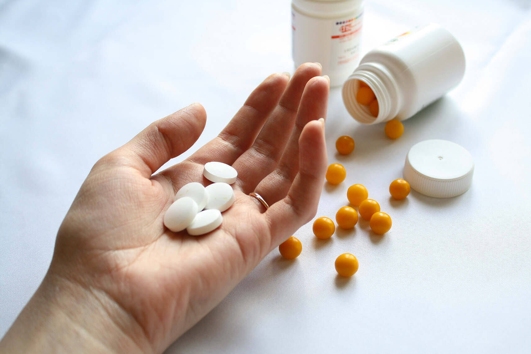 Hand holding white pills with orange pills and medication bottles in background for addiction treatment