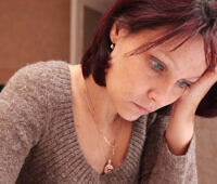 Middle-aged woman with red hair looking distressed, holding her head in her hand, depicting signs of anxiety or depression