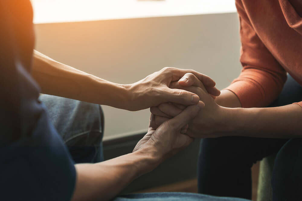 Close-up of two people holding hands in a supportive gesture, symbolizing empathy and connection during drug rehabilitation