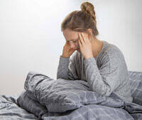 Young woman sitting in bed holding her head, appearing to suffer from headache or discomfort during drug withdrawal