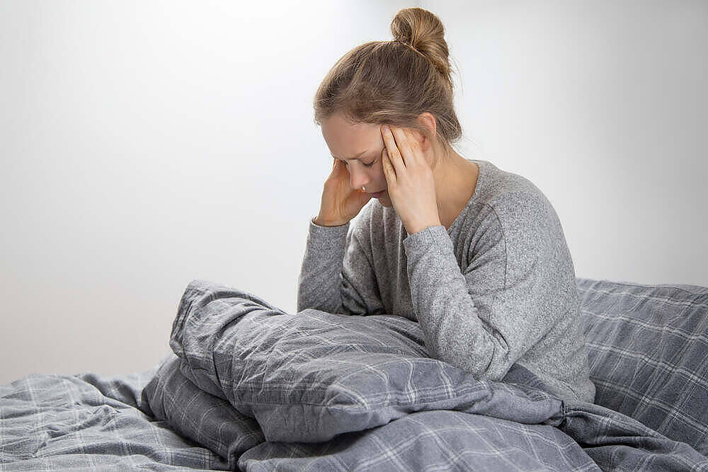 Young woman sitting in bed holding her head, appearing to suffer from headache or discomfort during drug withdrawal