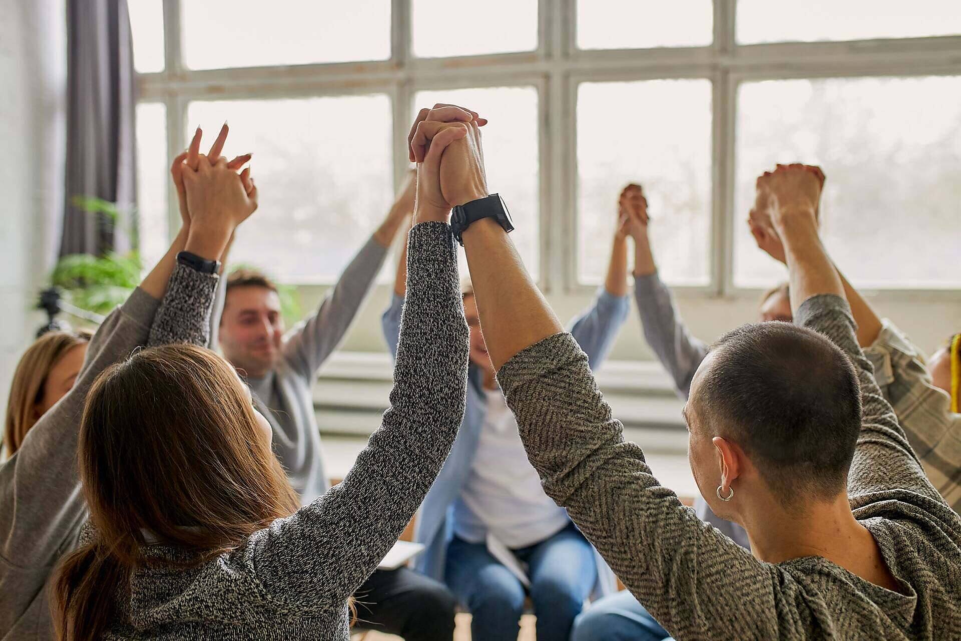 People in alcohol rehab raising joined hands in celebration during a group therapy session, symbolizing unity and success in recovery