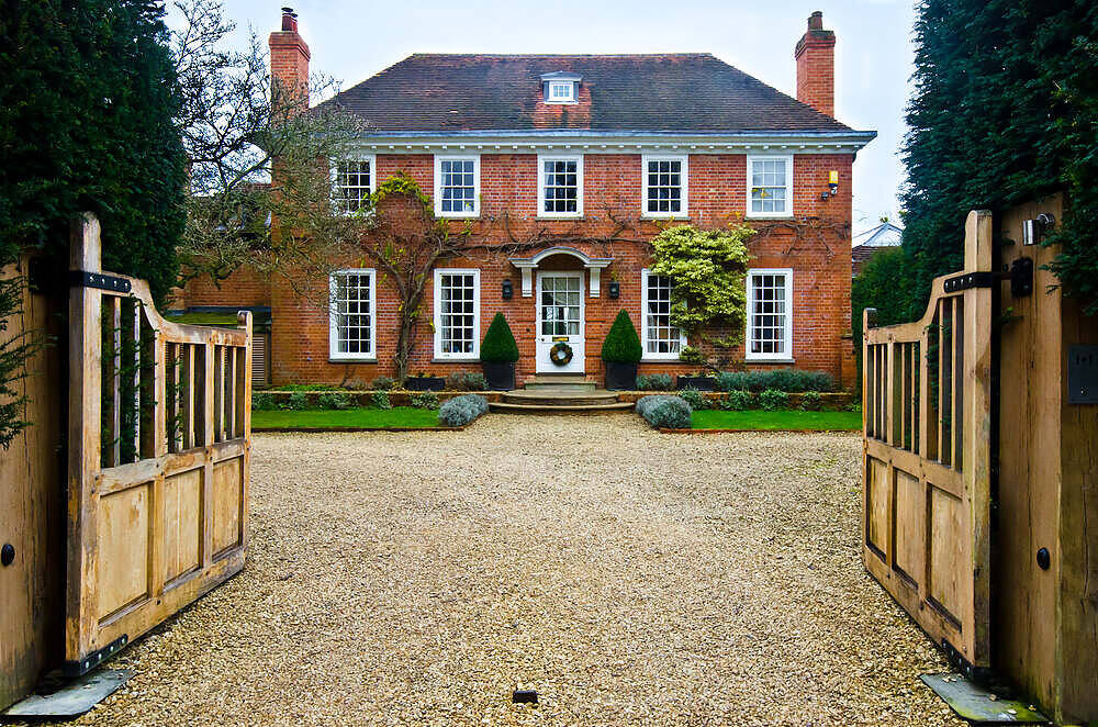 Elegant brick Georgian-style manor house with manicured gardens, perfect for luxury drug and alcohol rehabilitation, viewed through ornate wooden gates