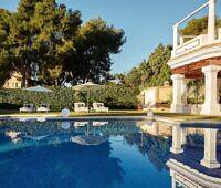 Serene swimming pool surrounded by lounge chairs and umbrellas at a luxury rehab resort, with elegant white columns and lush greenery