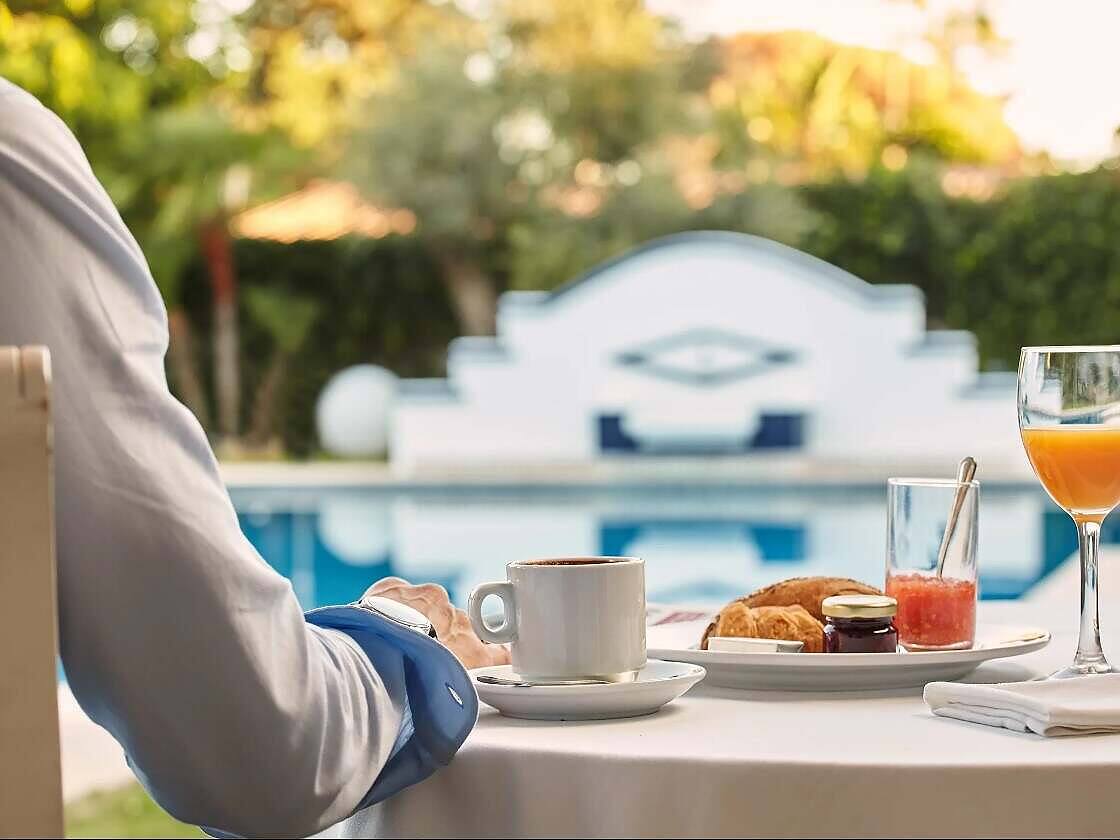 Elegant poolside breakfast setting at a luxury rehab facility, featuring coffee, croissants, juice, and a serene swimming pool backdrop