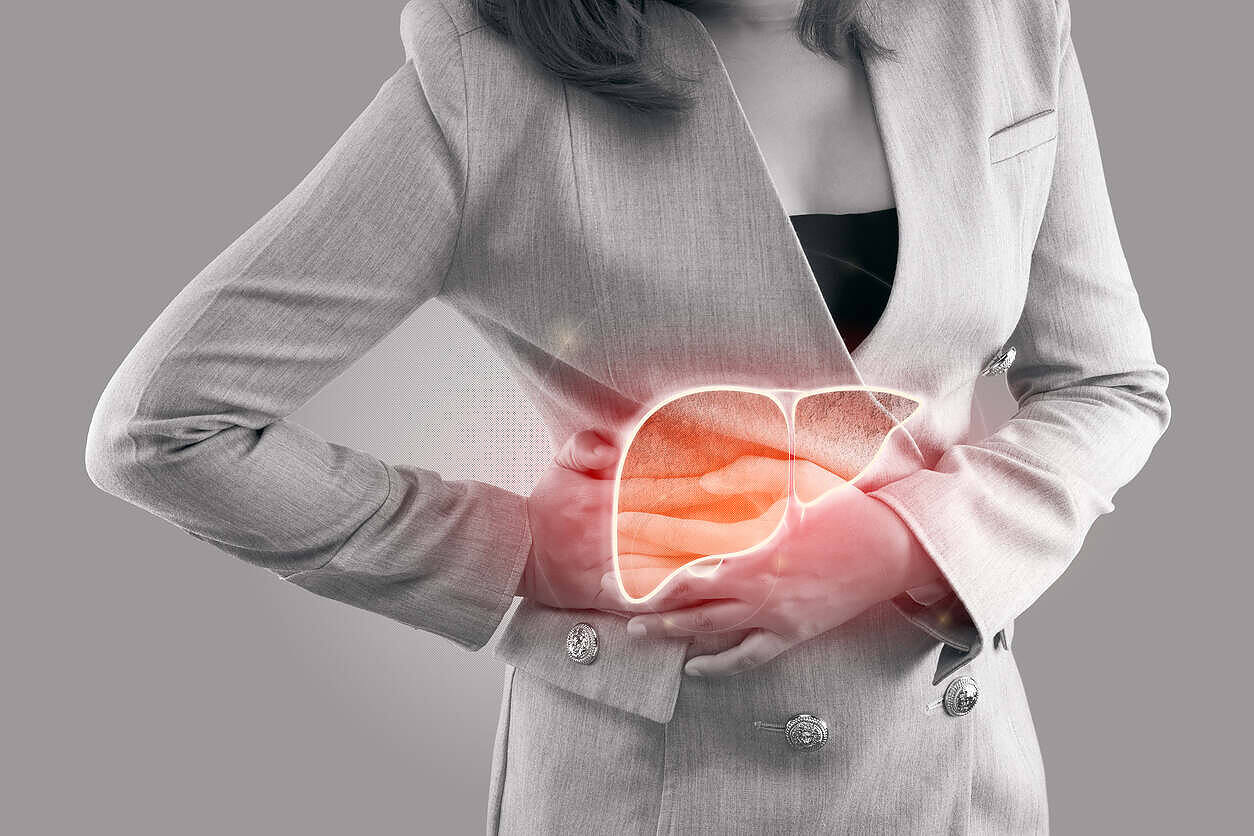 Woman in grey suit holding her side with a glowing illustration of a liver, depicting alcohol-related liver pain and damage