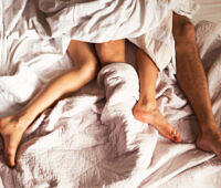 Legs of a couple intertwined in rumpled white bedsheets, suggesting intimate activity