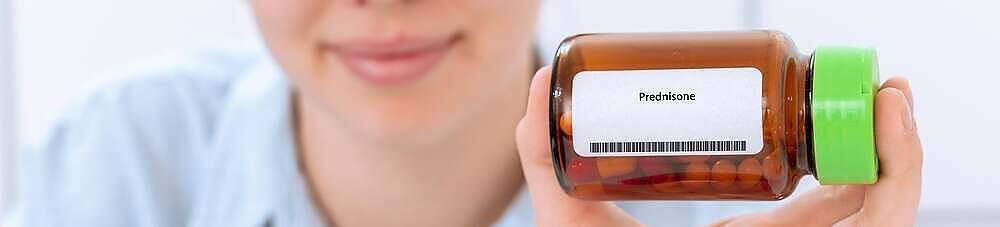 Close-up of a healthcare worker's hand holding a prescription bottle labeled Prednisone