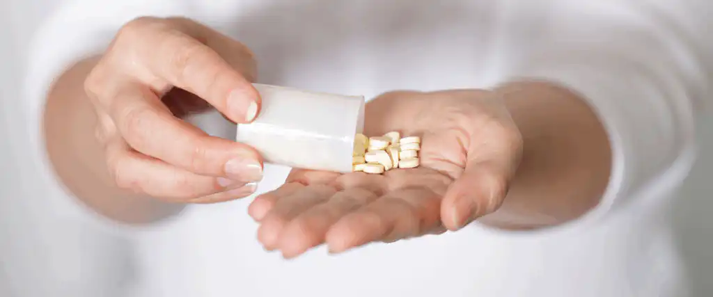 Woman holding tub of pills pouring them out into her hand