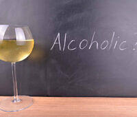 A glass of white wine next to a chalkboard with 'Alcoholic?' written on it, suggesting self-reflection on drinking habits