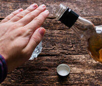 Hand gesture refusing alcohol, blocking whiskey bottle on wooden table, symbolizing quitting drinking