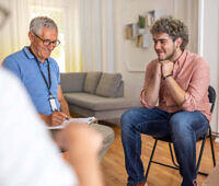 Therapist conducting an individual counseling session with a young man in a comfortable rehab facility setting