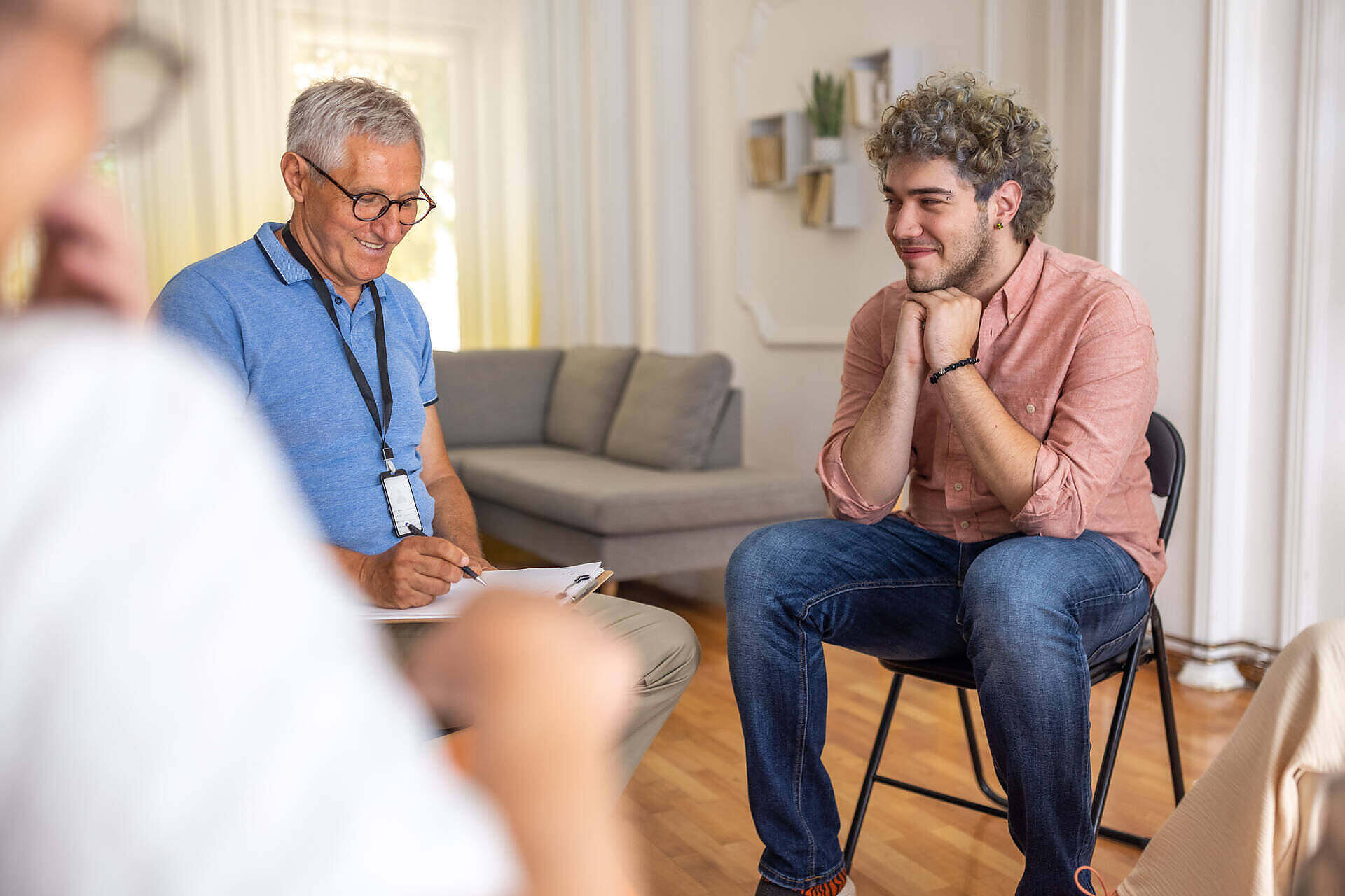 Therapist conducting an individual counseling session with a young man in a comfortable rehab facility setting