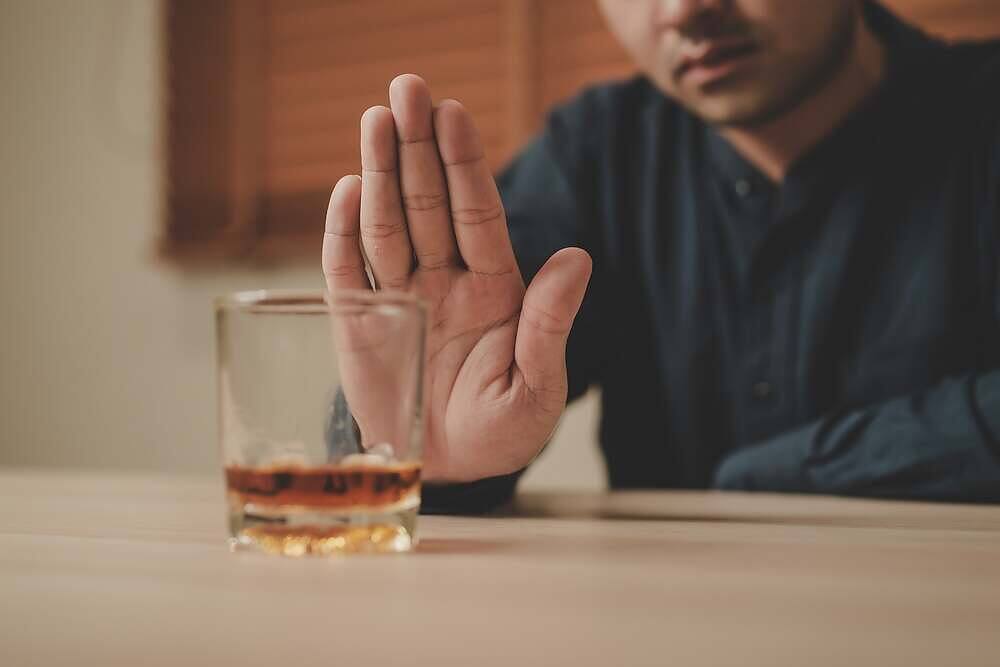 Man holding up hand in refusal gesture towards a glass of whiskey, indicating potential alcohol dependency awareness