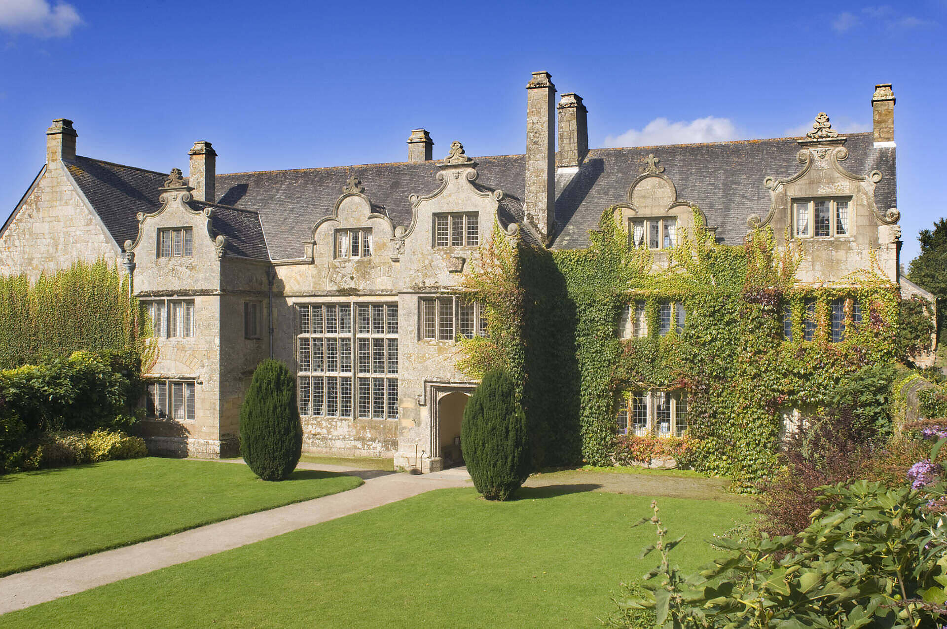 Majestic stone manor house with ornate windows, ivy-covered walls, and well-manicured gardens in the English countryside