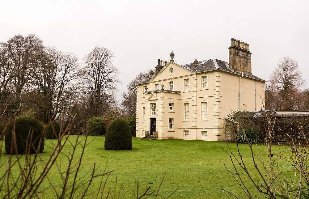 Elegant yellow manor house surrounded by manicured grounds and trees, ideal for peaceful addiction recovery