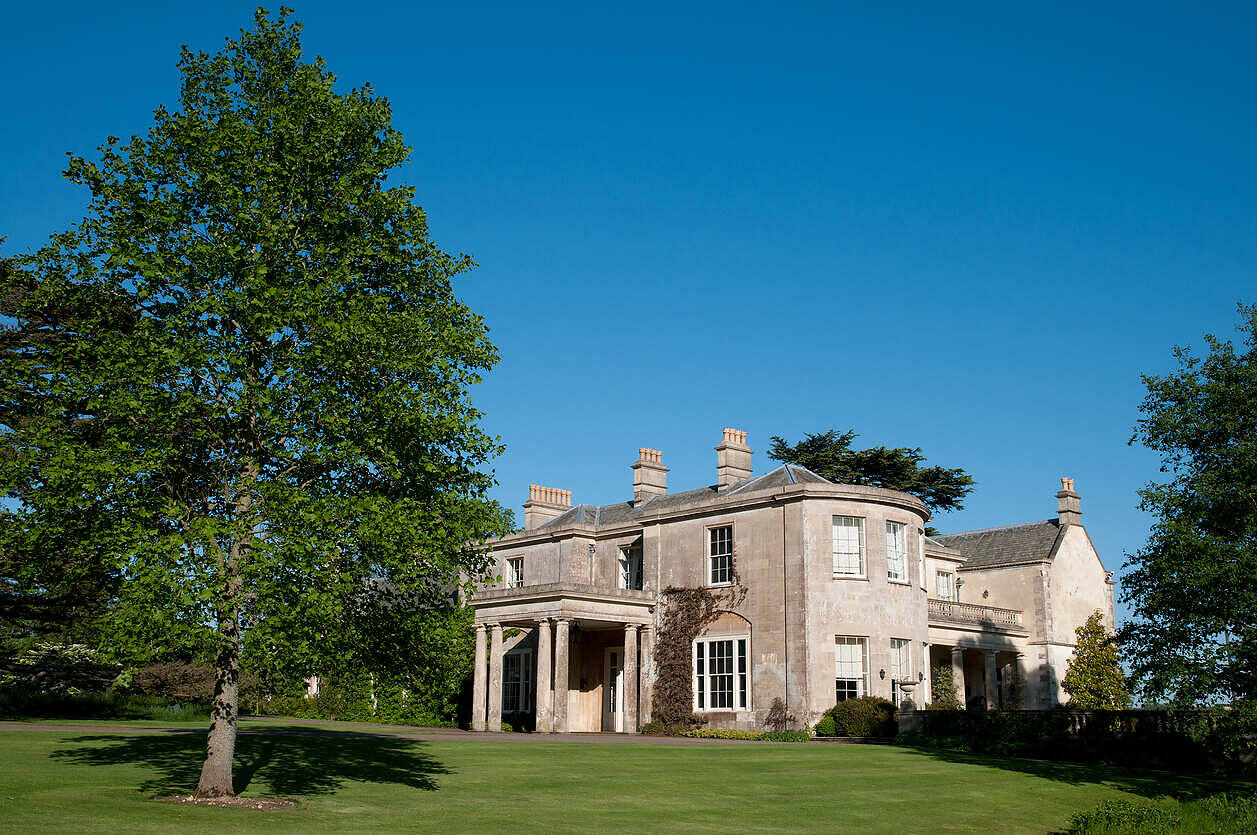 Elegant stone manor house with green lawns and trees, ideal for upscale rehab in Scotland