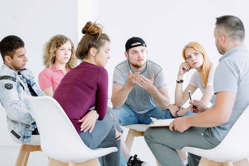 Diverse group of young adults in a therapy session, discussing substance abuse issues and recovery strategies