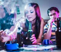 Young woman drinking alcohol and smoking at a party, surrounded by beer bottles and cigarettes, illustrating teenage substance abuse