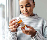 Woman in striped shirt examining orange prescription bottle, likely containing anti-craving medication for alcohol treatment