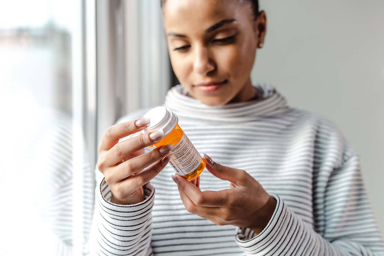 Woman in striped shirt examining orange prescription bottle, likely containing anti-craving medication for alcohol treatment