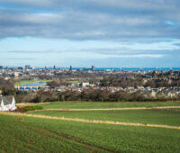 Panoramic view of Aberdeen city skyline with countryside fields in foreground, showcasing urban and rural Scotland
