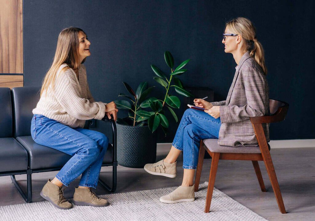 a woman sitting in chairs talking to another woman