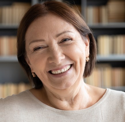 Smiling mature woman in white sweater in front of bookshelves