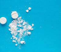 White pharmaceutical pills and powder scattered on bright blue surface, representing opioid medications