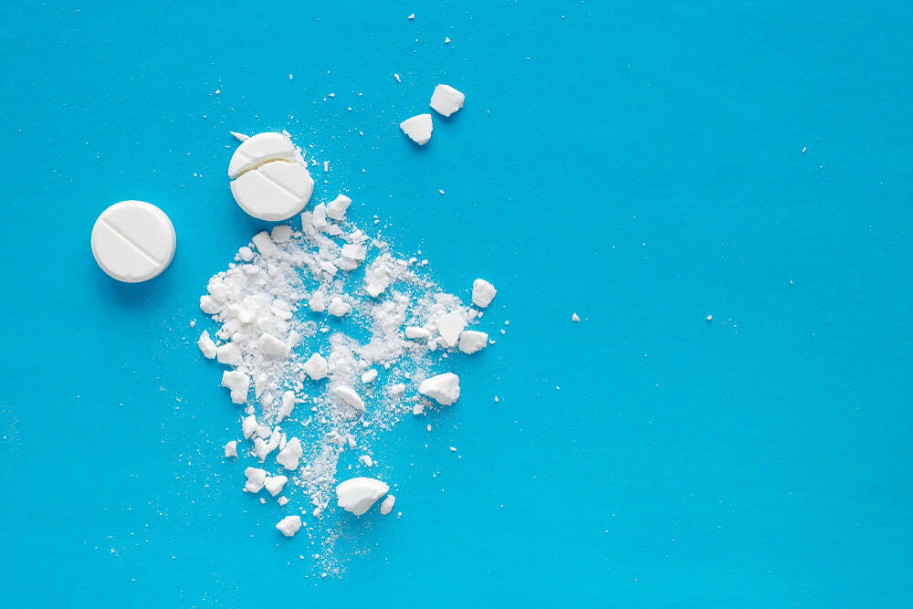 White pharmaceutical pills and powder scattered on bright blue surface, representing opioid medications